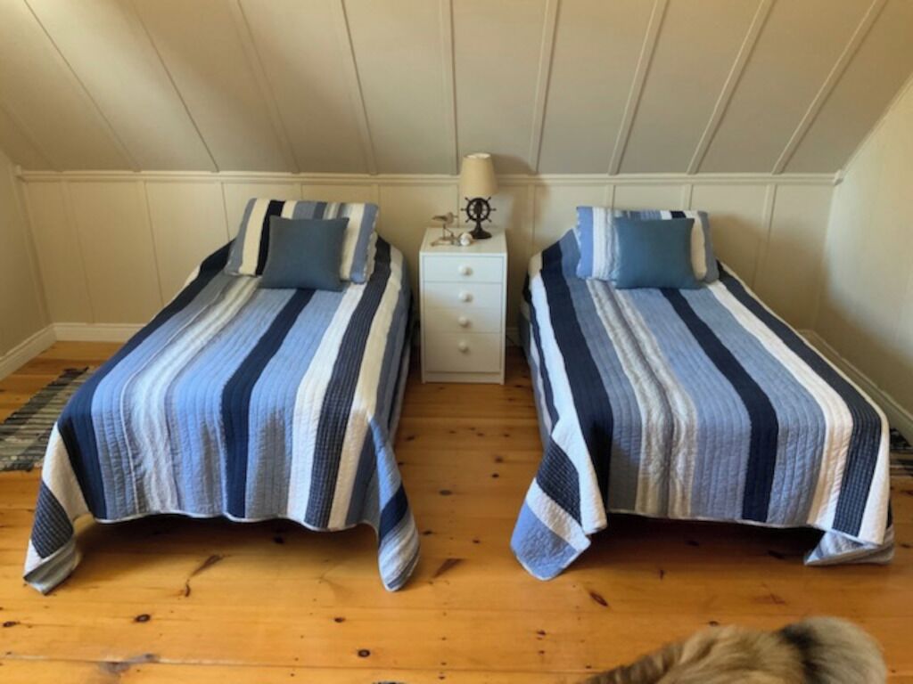 Una habitación con dos camas individuales, una mesita de noche con lámpara y suelo de madera.