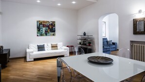 A modern living room with a white sofa, a dining table with chairs, a clear glass coffee table, and a colorful abstract painting on the wall. - Agata Apartment with Balcony by Wonderful Italy (Catania)