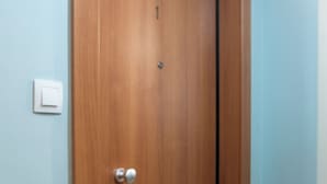 A wooden door with a silver handle, a light switch on the wall, and a tiled floor.