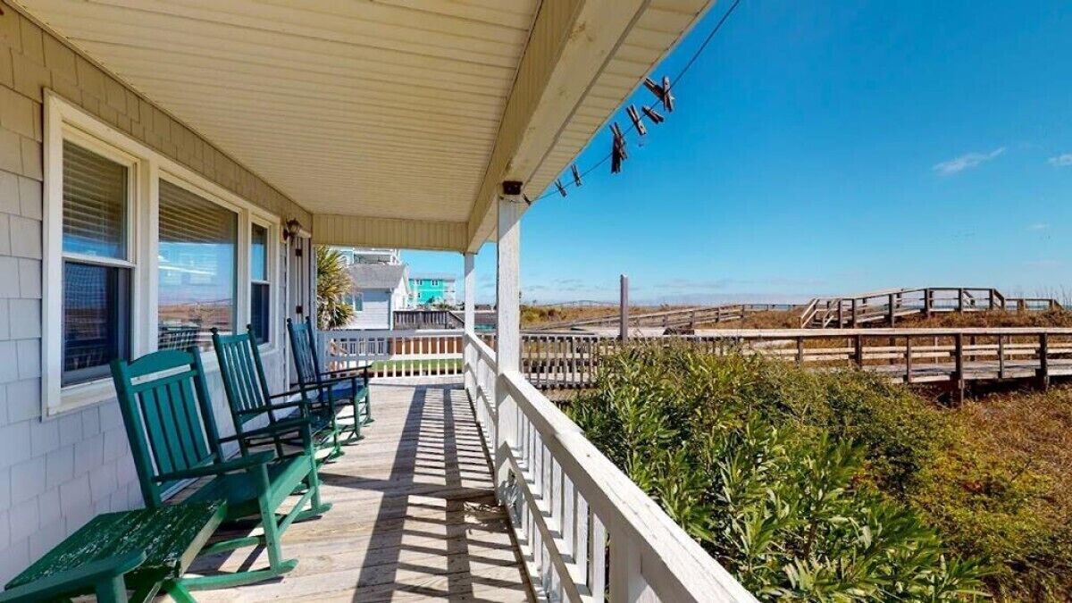 Eine überdachte Veranda mit grünen Bänken und Blick auf den Strand sowie ein hölzerner Steg.
