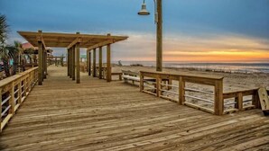 Une promenade en bois menant à une plage, avec une pergola en bois et des bancs.