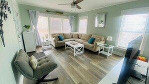 Ein Wohnzimmer mit einer Sofagarnitur, einem Couchtisch, einem Fernseher und einem Deckenventilator.