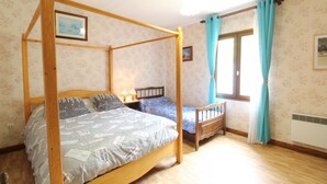 Una cama con dosel de madera, una cama individual más pequeña y una ventana con cortinas.