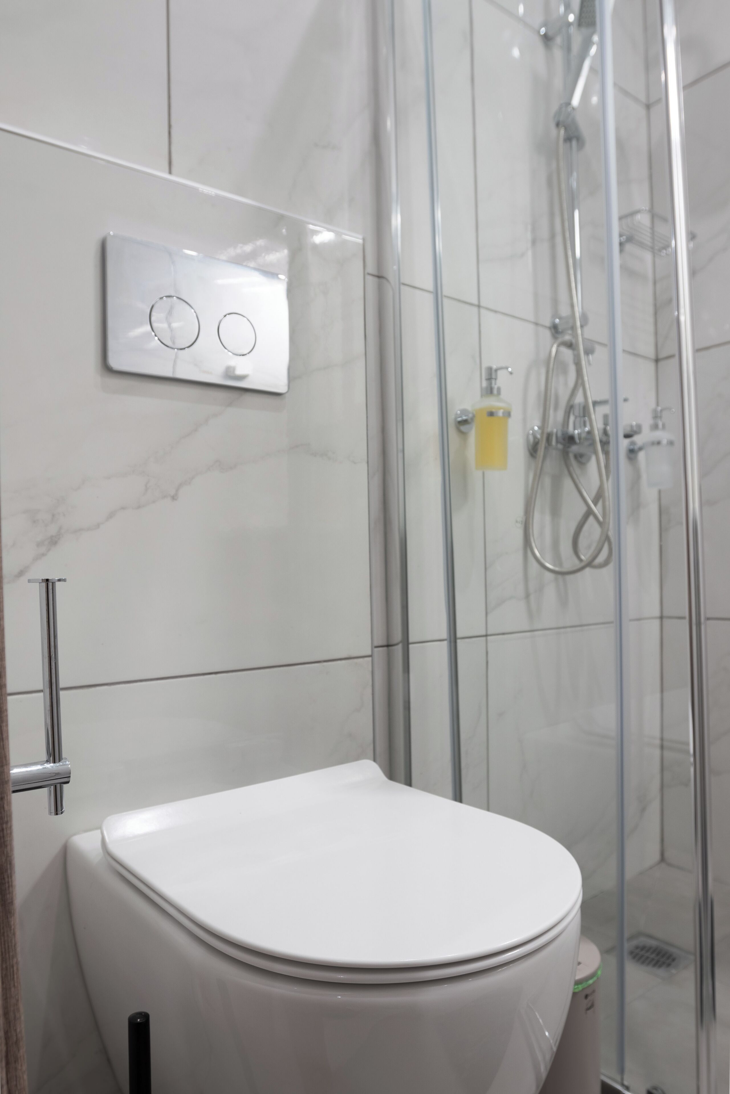 Et moderne badeværelse med et hvidt toilet, en brusekabine med glasvægge og et panel til betjening på væggen.