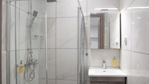 Un bany modern amb dutxa de vidre, un lavabo blanc i un mirall sobre el lavabo.