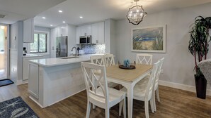 Una cocina moderna con muebles blancos, una isla central y un comedor con sillas blancas.