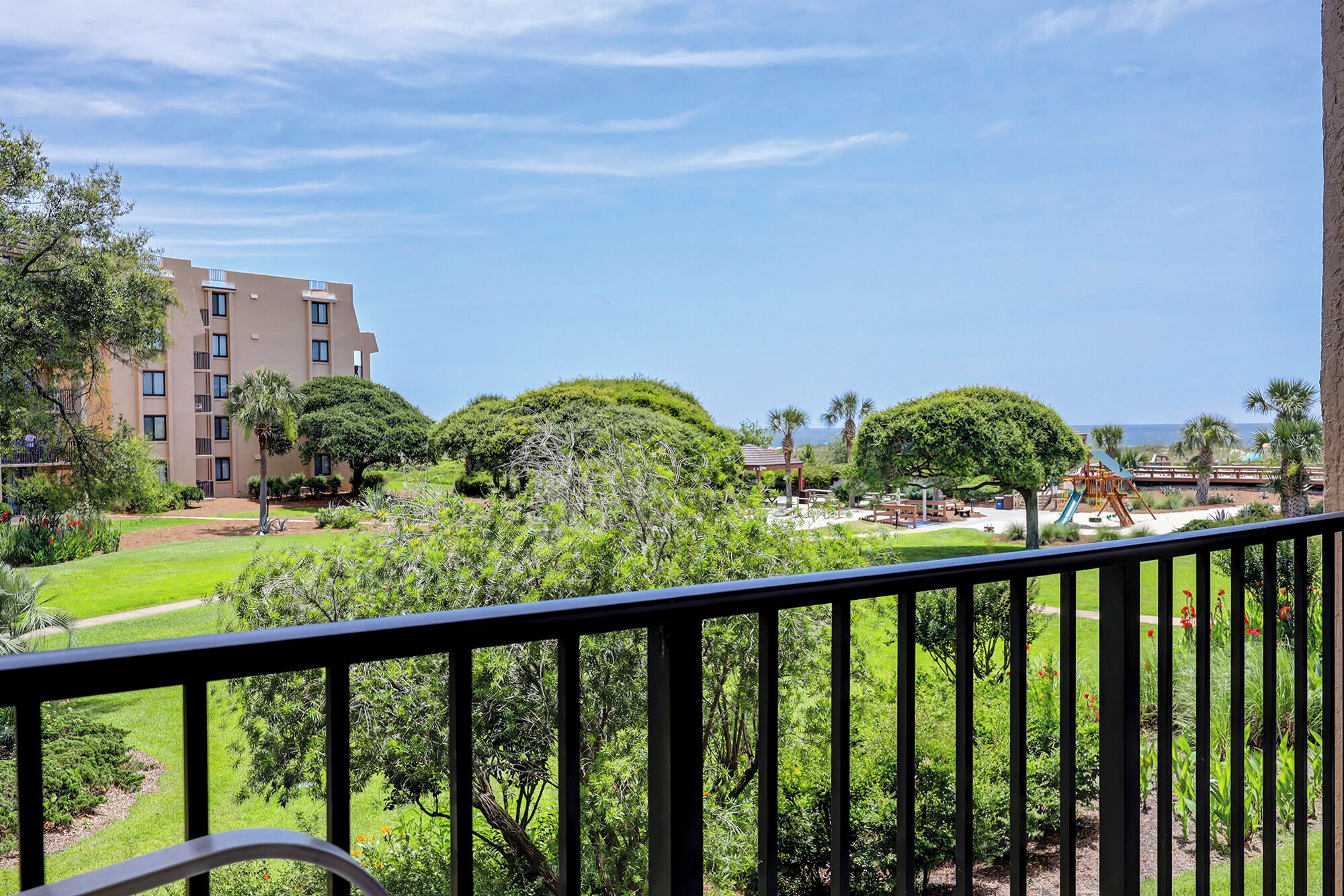 A balcony with a view of a landscaped garden, a playground, and a building with multiple floors.