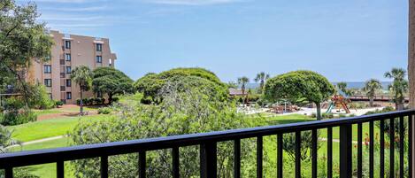 A balcony with a view of a landscaped garden, a playground, and a building with multiple floors.
