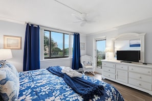 A bedroom with a large bed, a television, a chair, and a balcony. - 4203 Island Club - Folly Field - 2 Bed 2 Bath Sleeps 5 - Hilton Head Rentals (Hilton Head Island)