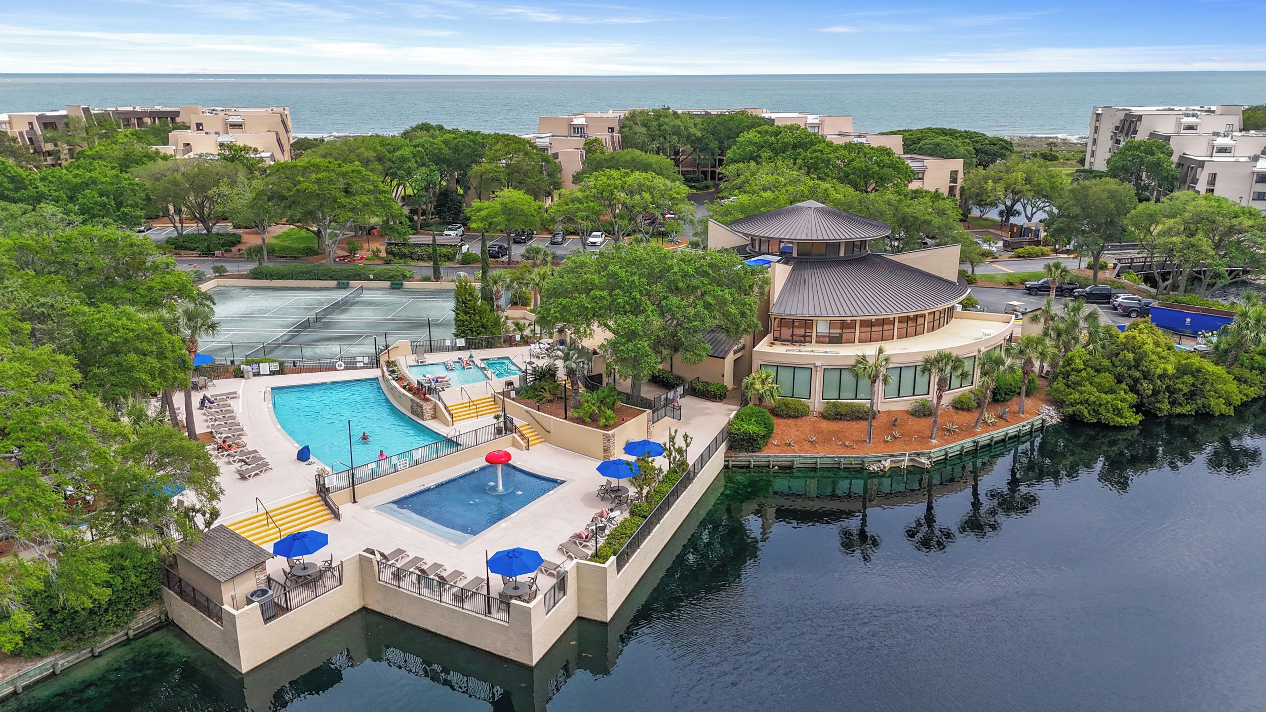 A resort with a central pool, a tennis court, and a view of the sea.