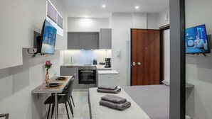 A compact hotel room with a bed, a small dining table with chairs, a kitchenette, and a TV mounted on the wall. - Pagrati Studio New Chic and Central (Athens)