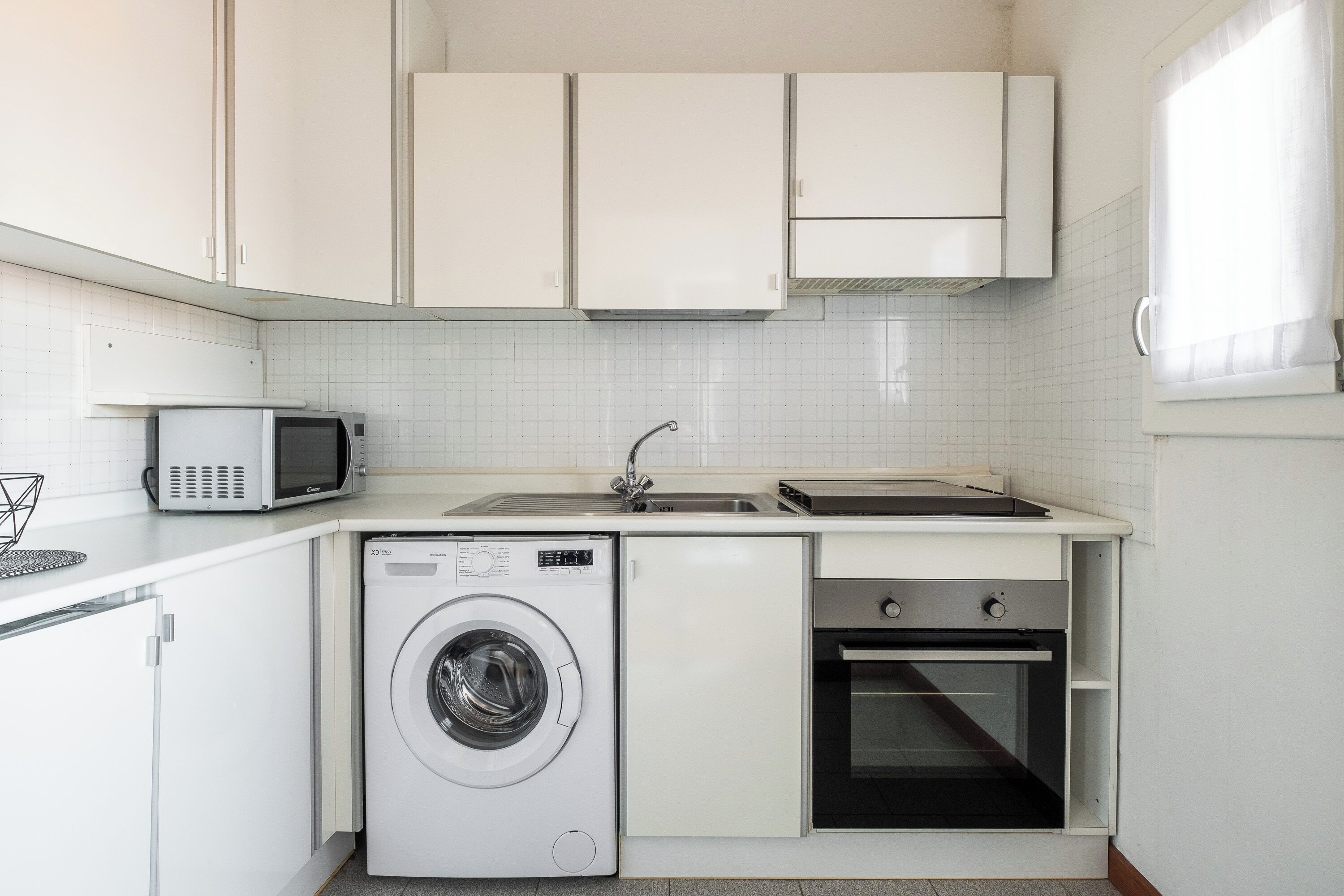 A compact kitchen with a washing machine, microwave, and oven.