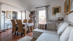 Een moderne woonkamer met een bank, eettafel, rieten stoelen en een boekenkast.