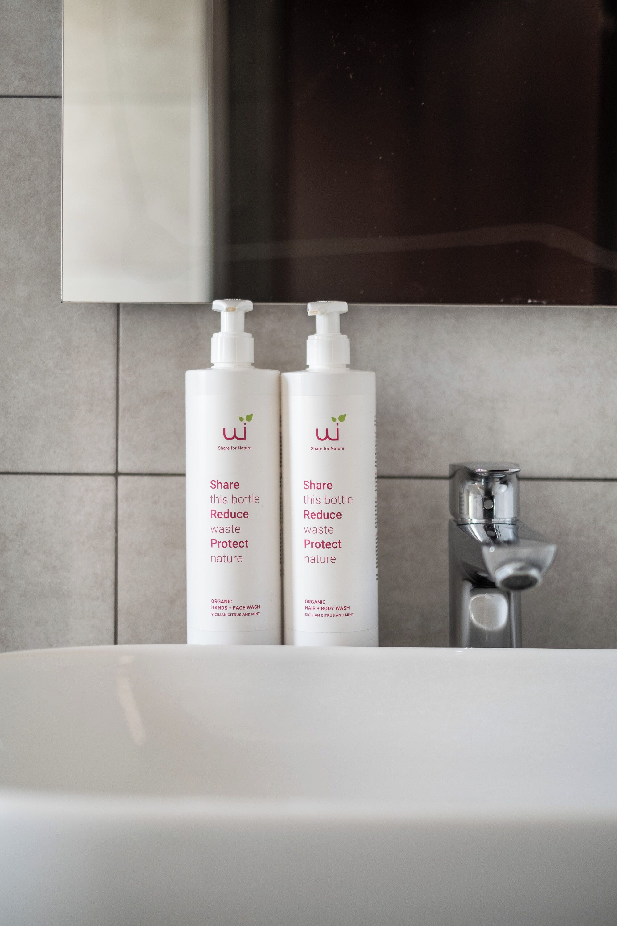 Two white bottles of organic face wash on a bathroom sink with a modern faucet.