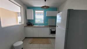 A compact kitchen with white cabinets, a sink, a stove, and a refrigerator. - Le Soleil Bleu, Charmant T2 à Proximité des Plages, Restaurants et Commerces (Le Gosier)