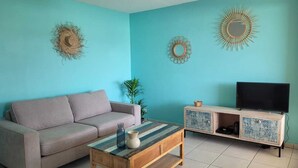 A living room with a sofa, coffee table, TV stand, and decorative wall art. - Le Soleil Bleu, Charmant T2 à Proximité des Plages, Restaurants et Commerces (Le Gosier)