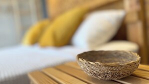 A woven basket on a wooden table in a room with a bed and pillows in the background.