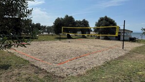A volleyball court with net, surrounded by trees and a building in the background.