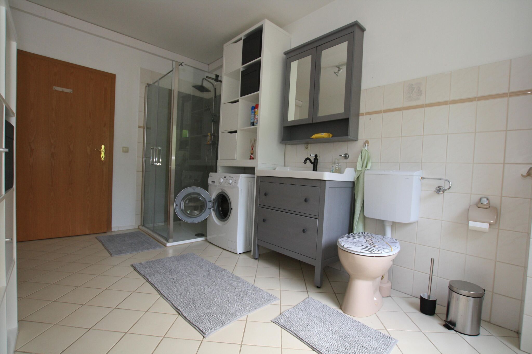Een moderne badkamer met een glazen douche, een wasmachine, een toilet en een wastafel.