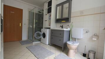 Een moderne badkamer met een glazen douche, een wasmachine, een toilet en een wastafel.