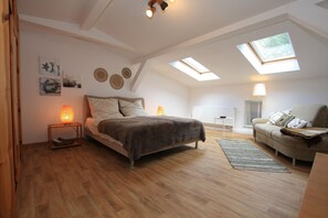 A bedroom with a bed, a sofa, a lamp, a rug, and a skylight.
