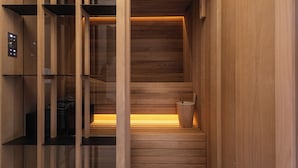 A sauna with wooden walls and a glass door, a control panel, and a wooden bucket. - Naomi Nice  (Nice)