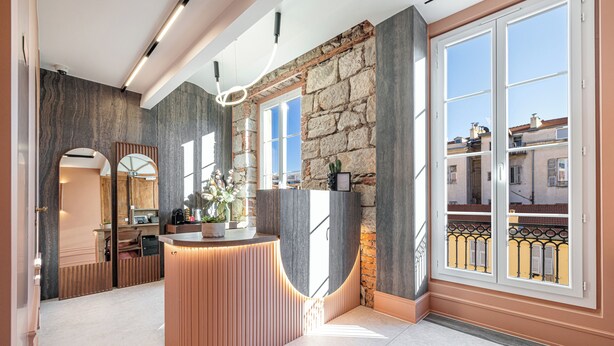 A reception area with a wooden reception desk, stone walls, and large windows with balconies. - Naomi Nice  (Nice)