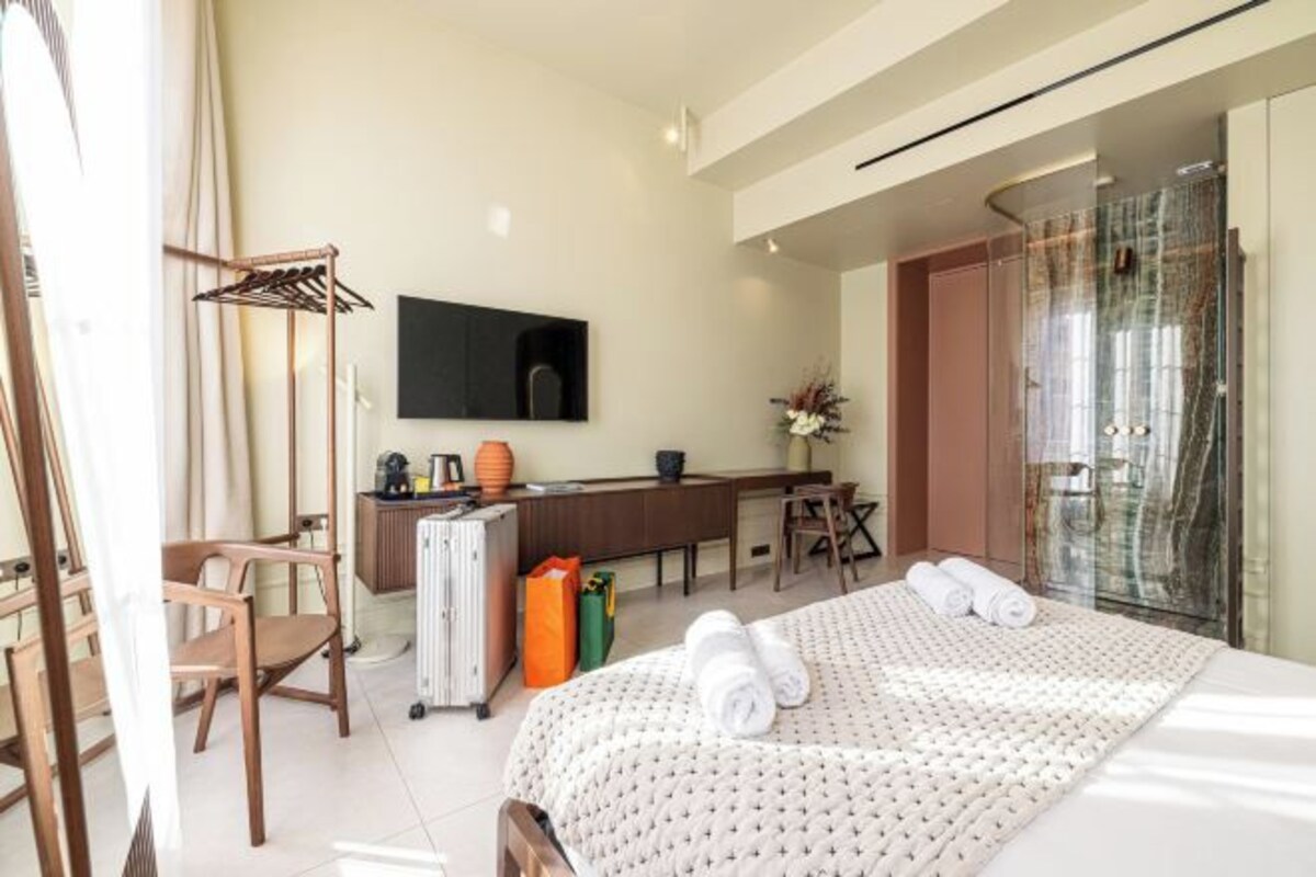 Une chambre d’hôtel équipée d’un lit, d’un bureau, d’une chaise, d’une télévision et d’une salle de bain avec une douche en verre.