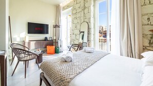 A hotel room with a bed, a TV, a desk, and a balcony with a stone wall. - Naomi Nice  (Nice)
