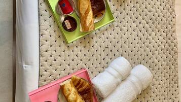 Un plateau de petit-déjeuner soigneusement préparé, avec des croissants, des tranches d’orange et une bouteille de jus, posé sur un lit recouvert d’une courtepointe matelassée.