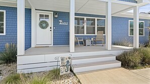 Een huis met een overdekte veranda, een voordeur versierd met een krans, en een bordje met de tekst 'Hello Summer'.