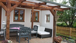 Ein Außenbereich mit Holz-Pergola, Tisch und Stühlen sowie einer gepolsterten Bank.