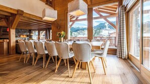 Un coin repas en bois, avec une grande table et des chaises, un luminaire suspendu et une vue sur l’extérieur.
