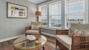 A cozy room with wicker furniture, a glass coffee table, and a view of the water through large windows. - Gorgeous sunset views looking over the waterway! 4BR/2.5Bath (Wrightsville Beach)