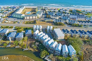 An aerial view of a coastal residential area with multiple houses and a large building, likely a hotel or resort, near the beach.