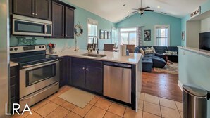 A modern kitchen with a central island, stainless steel appliances, and a dining area with a sofa and table. - Melon Camp - Dive into Fun with Pool Access! (Surf City)