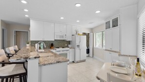 Una cocina moderna con armarios blancos, encimera de granito y comedor con mesa dispuesta para dos.