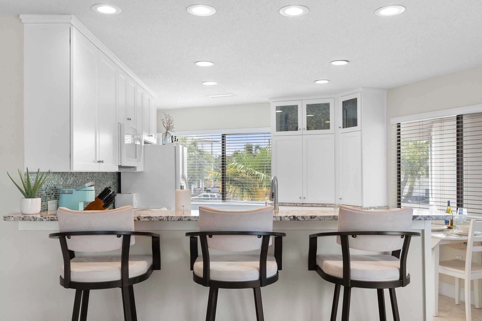 A modern kitchen with white cabinets, a marble countertop, and three bar stools.