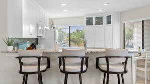 Una cocina moderna con armarios blancos, encimera de mármol y tres taburetes de bar.
