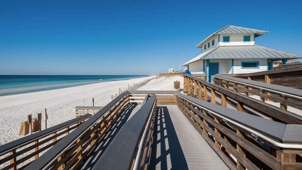 Una pasarela de madera que lleva a una playa, con un edificio al fondo.