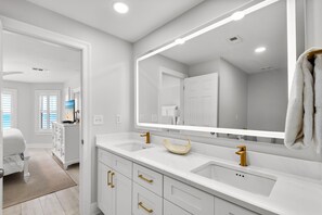 Un bagno moderno con mobili bianchi, maniglie dorate, uno specchio grande e un lavandino dalla forma particolare.