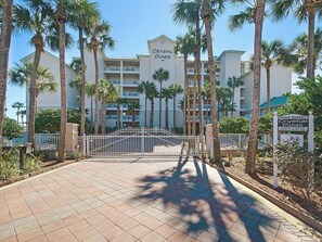 A multi-story hotel with a gated entrance, palm trees, and a clear sky.