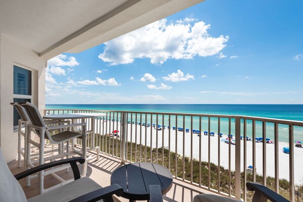 A balcony with a view of a beach, a table, and chairs.