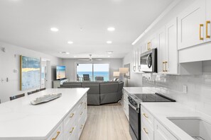 A modern kitchen with white cabinetry, a large island, and a view to the ocean.