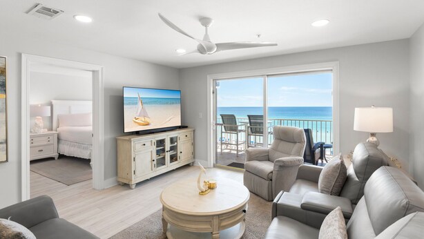 A spacious living room with a television, a round coffee table, a sofa, and a balcony with a view of the ocean. - Gulf Front Condo in Gated Complex and Seasonal Beach Service (Destin)