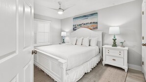 A bedroom with a bed, a nightstand, a ceiling fan, a painting, and a door. - Gulf Front Condo in Gated Complex and Seasonal Beach Service (Destin)