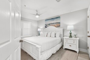 Una camera da letto con un letto, un comodino, una ventola a soffitto, un quadro e una porta.