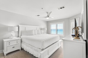 A bedroom with a bed, nightstands, a lamp, a ceiling fan, and a window with blinds.