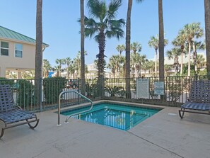 A pool area with a metal fence, two lounge chairs, and palm trees in the background.