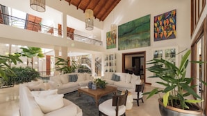 A spacious living area with a high ceiling, large windows, and a staircase leading to an upper floor.